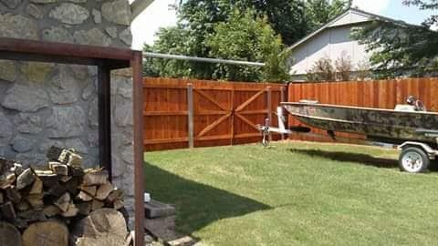 A boat is on a trailer in a backyard next to a pile of logs.