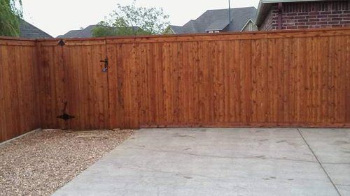 A wooden fence is surrounding a concrete driveway.