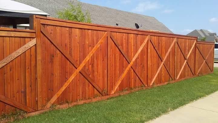 A wooden fence is sitting next to a sidewalk in front of a house.