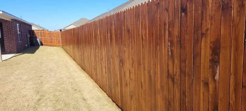 A long wooden fence surrounds a grassy yard in a backyard.