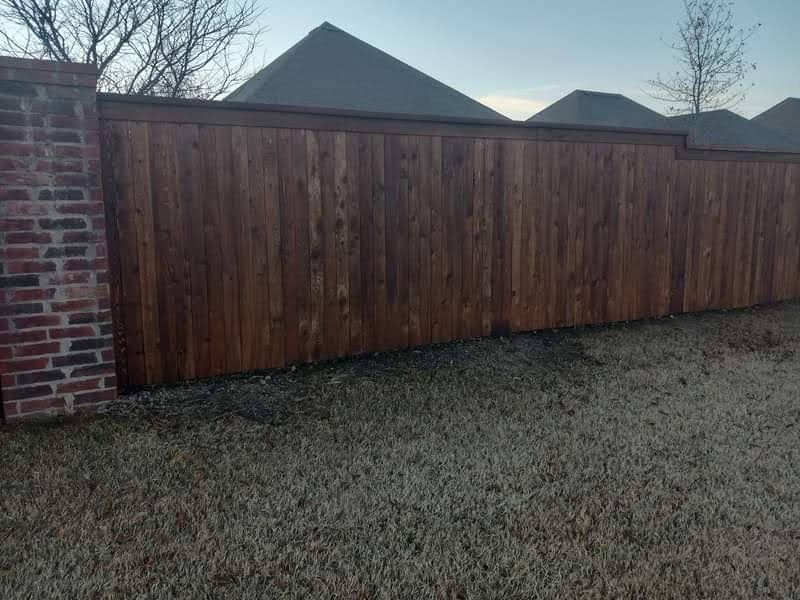 A wooden fence surrounds a brick wall in a backyard.