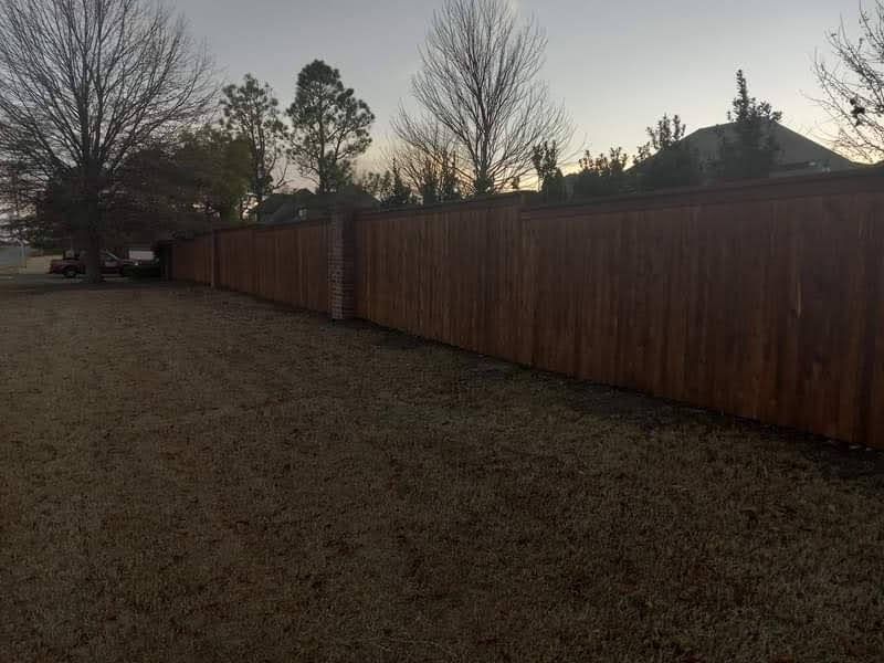 A wooden fence in a backyard with trees in the background.