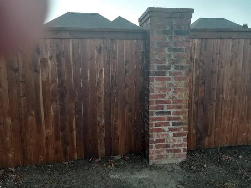 A wooden fence with a brick post in front of it.