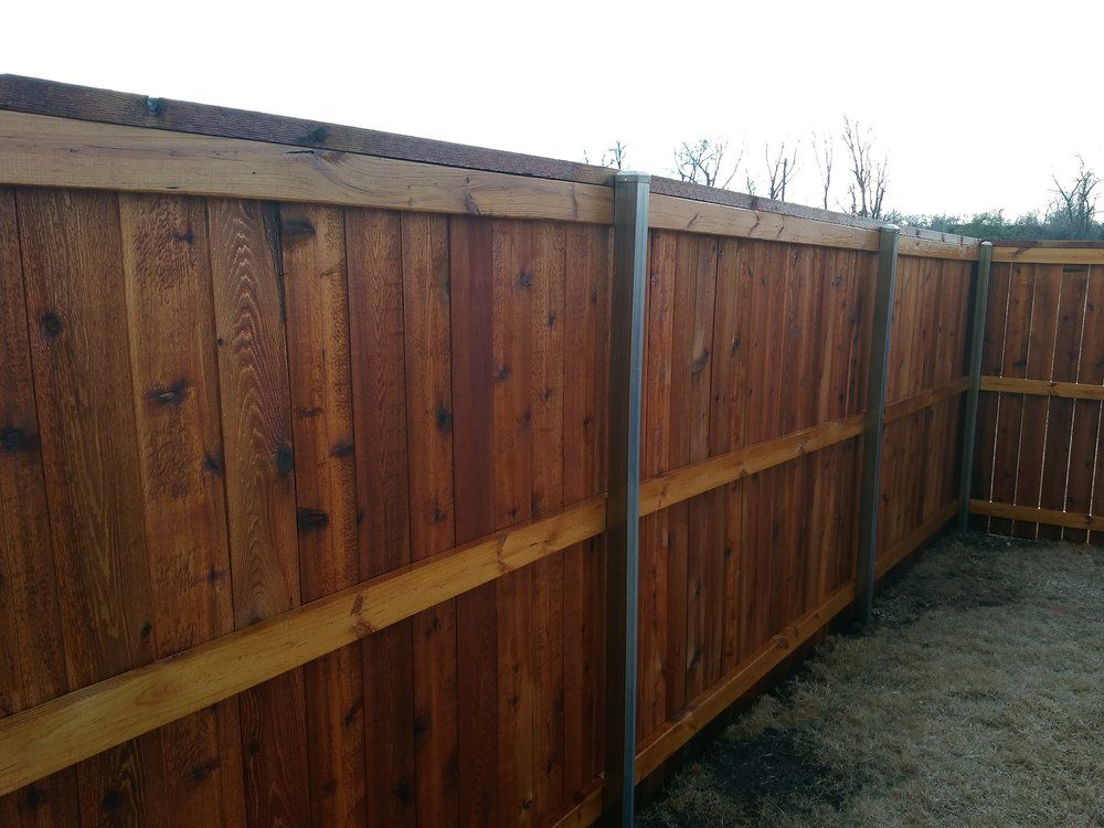 A wooden fence with a metal post in the middle of a yard.
