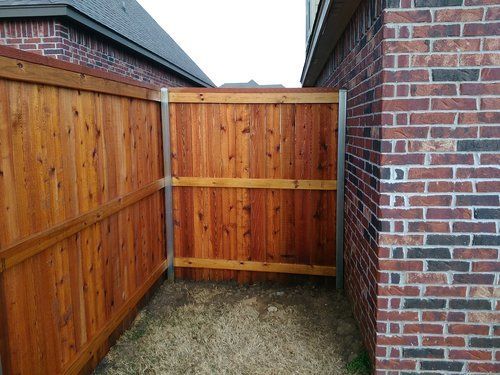 A wooden fence is between two brick buildings.