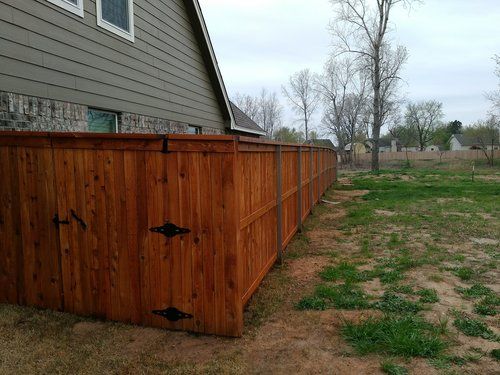 A wooden fence surrounds a grassy yard in front of a house.