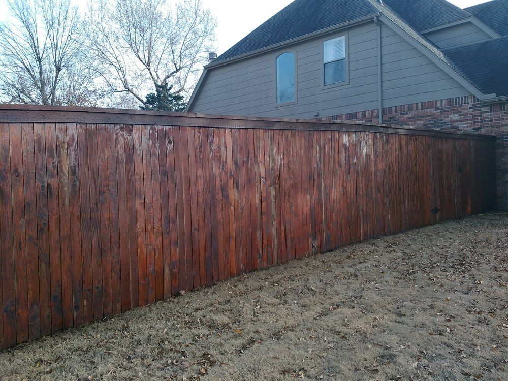 A wooden fence surrounds a backyard with a house in the background