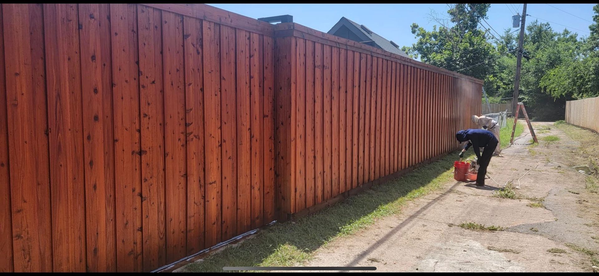 A man is painting a wooden fence on a dirt road.