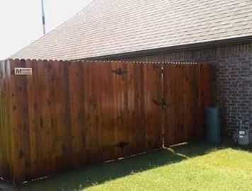 A wooden fence is sitting next to a brick building in a backyard.