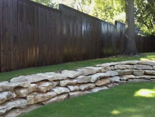 A wooden fence surrounds a stone wall in a backyard.