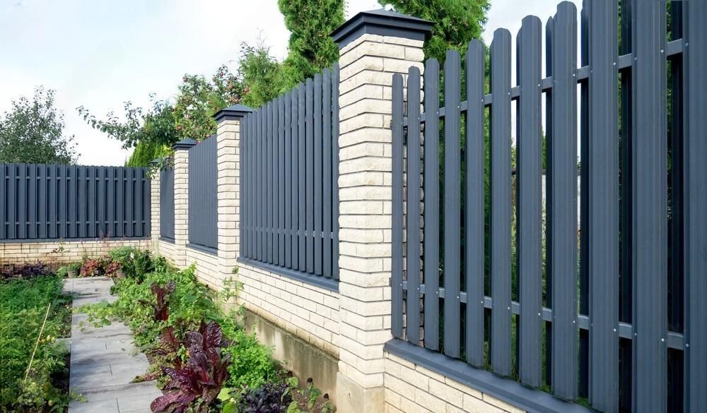 A fence made of wood and bricks surrounds a garden.