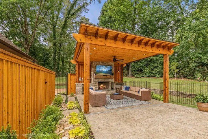 A wooden pergola with a fireplace and television underneath it.