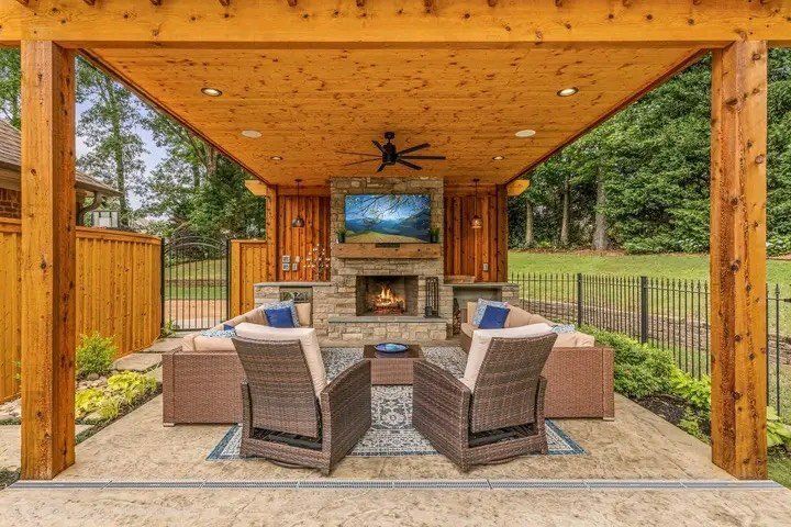 A patio with a fireplace , chairs , a table and a television.