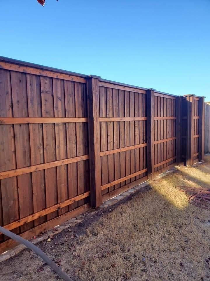 A wooden fence in a backyard with a blue sky in the background.
