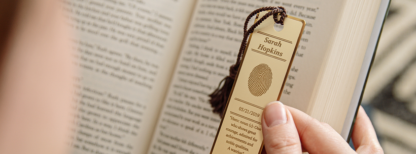 A person is holding a wooden bookmark over an open book.