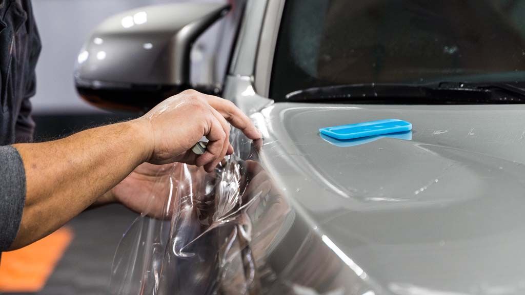 A man is applying protective film to the hood of a car.