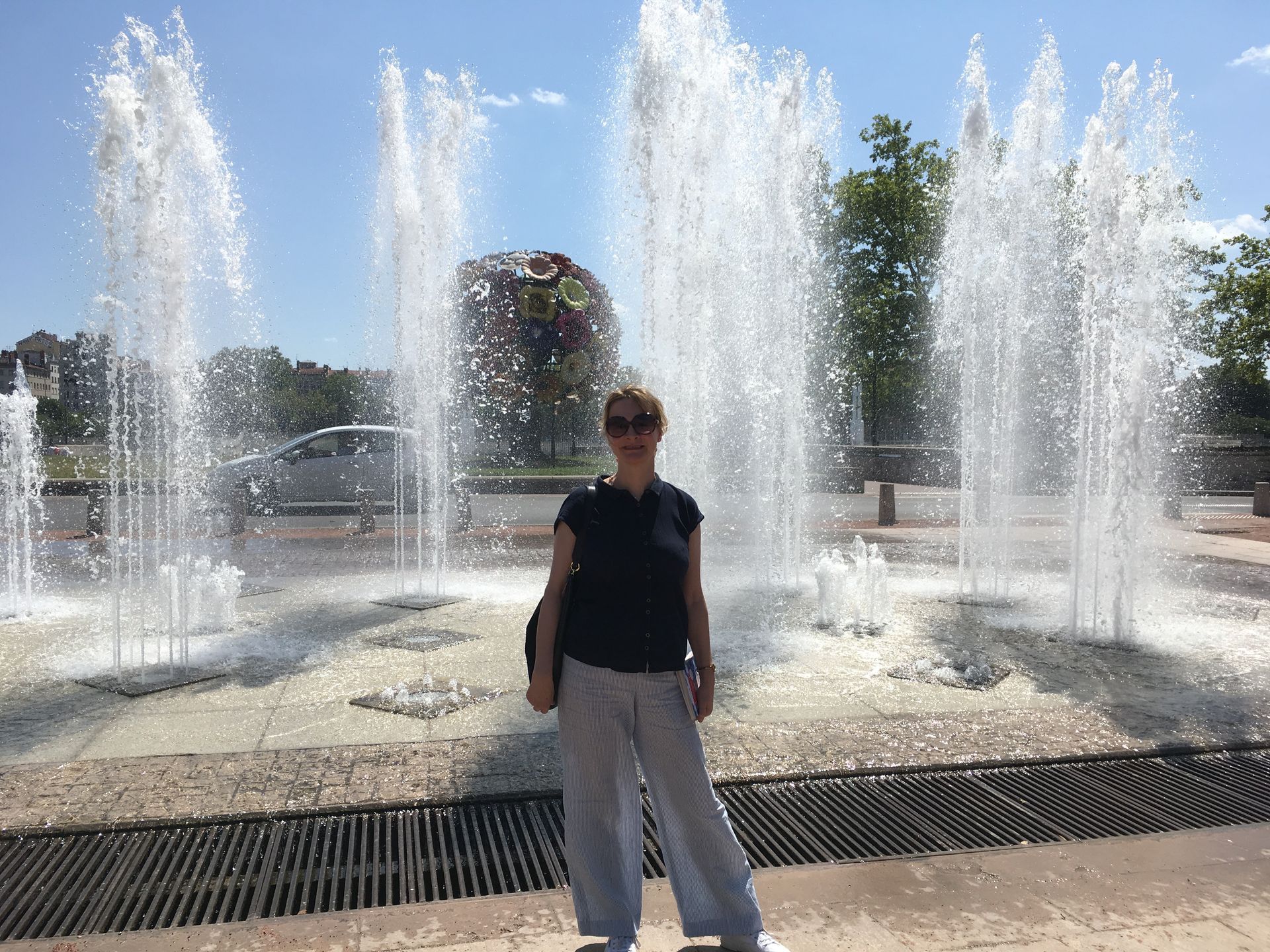 Woman standing in the sunlight in front of many tall fountains.