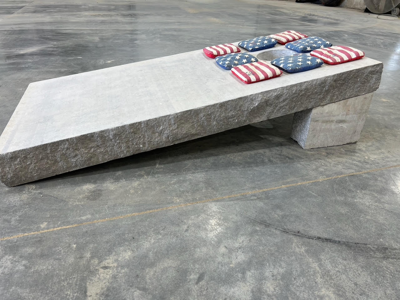 a custom cornhole board made out of stone with red, white, and blue bags on top.
