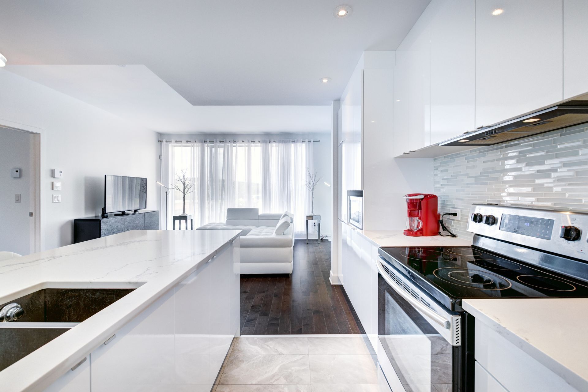 Bright modern kitchen with white counters, stainless appliances, and a dining area by large windows