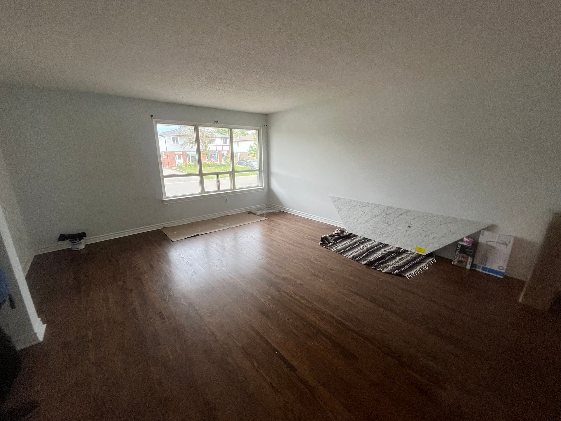Empty room with wood floors, white walls, and a large window letting in daylight.