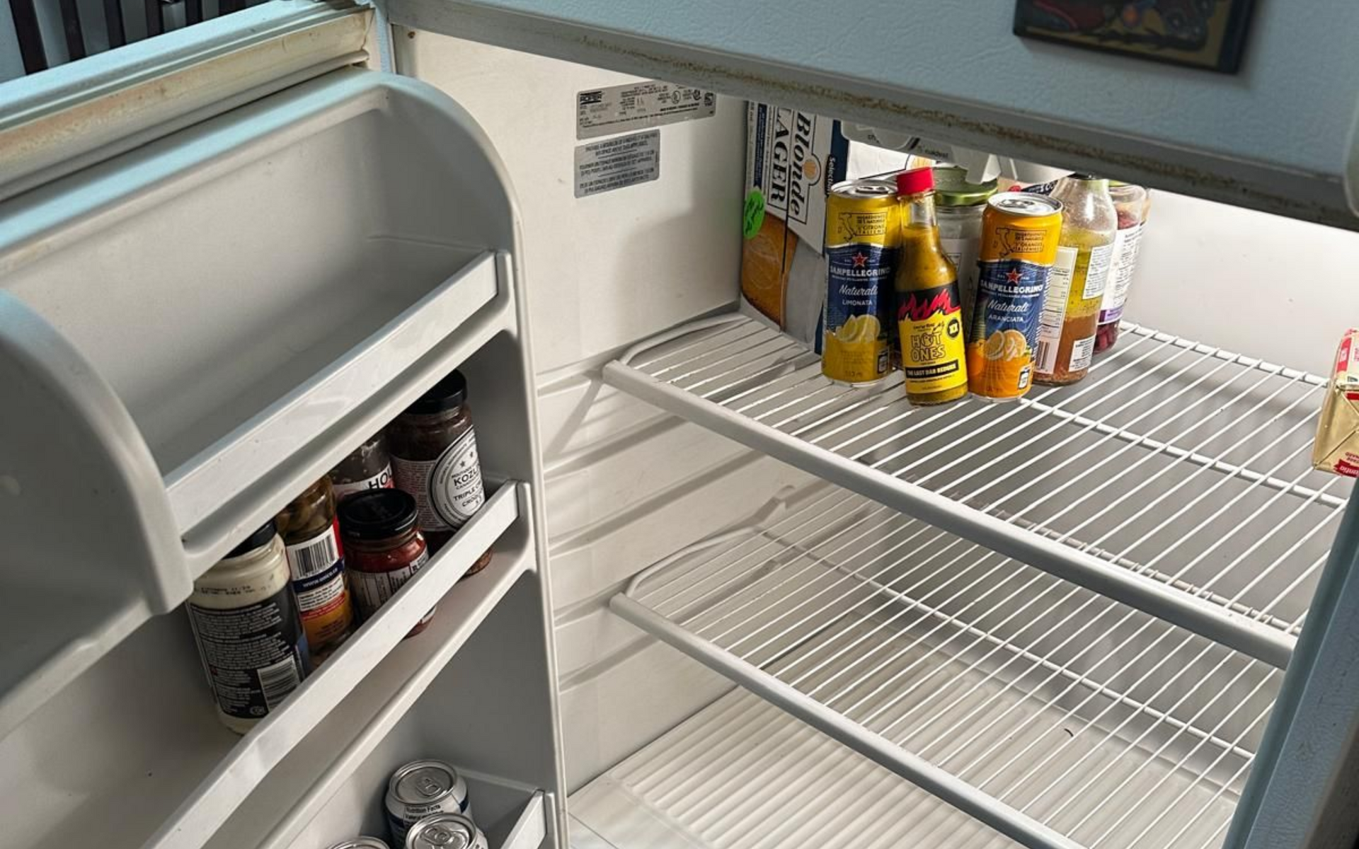 An open refrigerator with some drinks on the top shelf and jars on the door.
