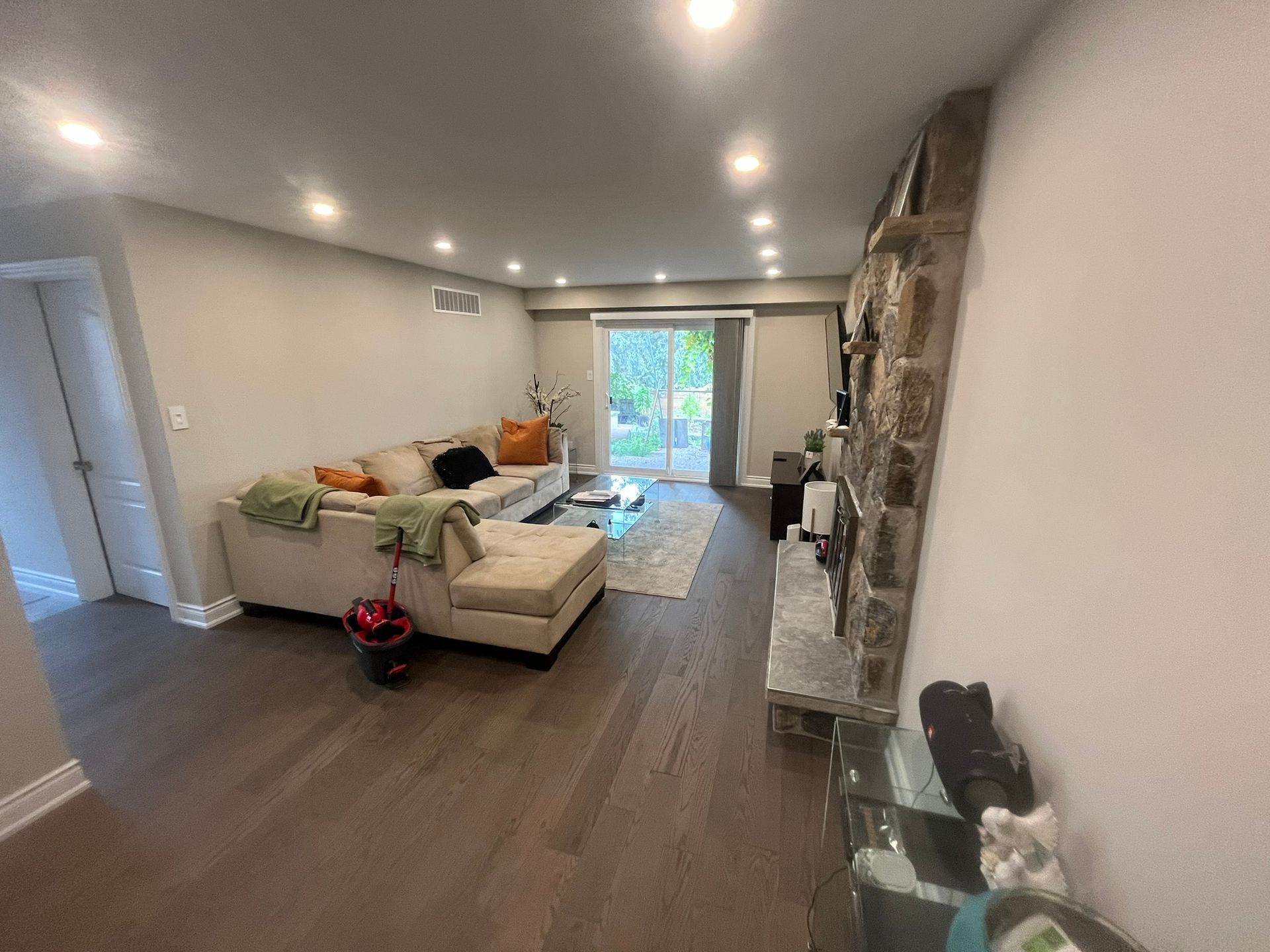 Living room with a stone fireplace, beige sectional, and sliding glass doors to a backyard.