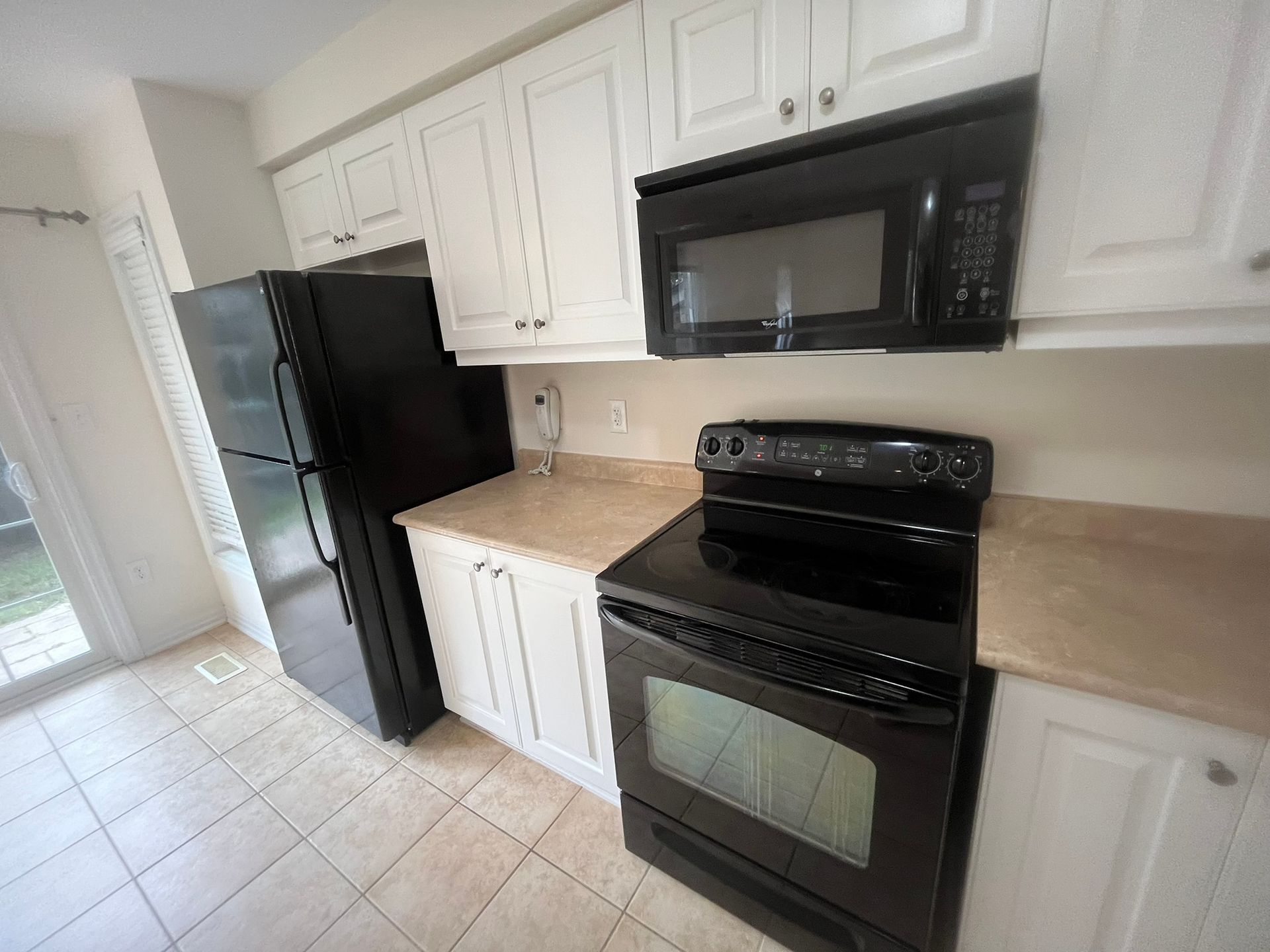 A kitchen with white cabinets , a black refrigerator , a black stove , and a black microwave.