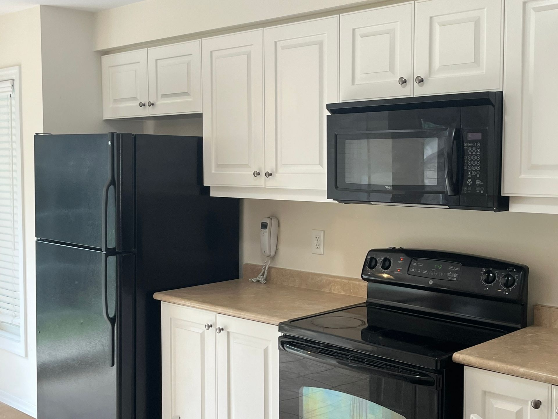 A kitchen with white cabinets , a black refrigerator , a black stove , and a black microwave.