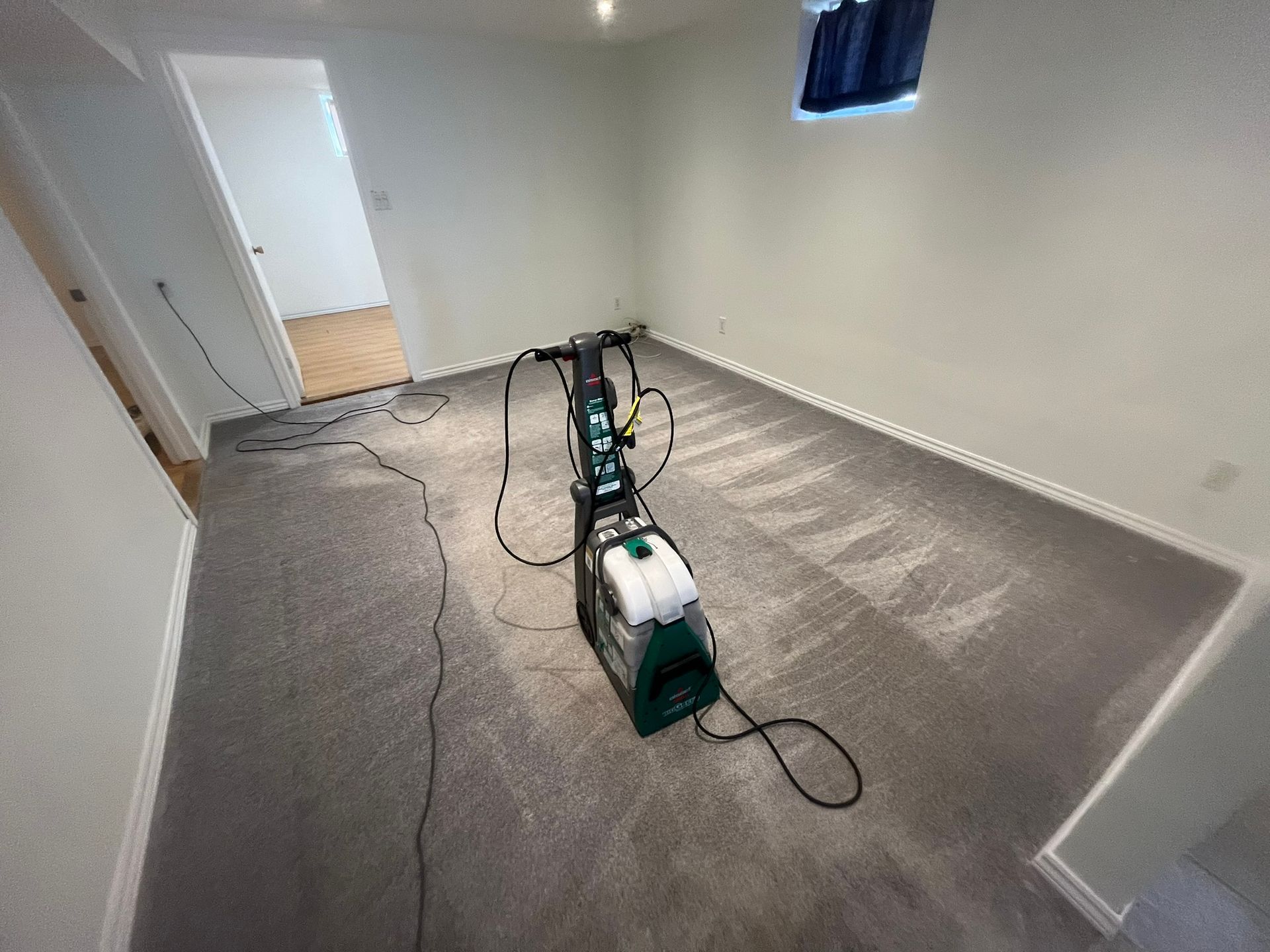 A carpet cleaning machine in a room with gray carpet, white walls.