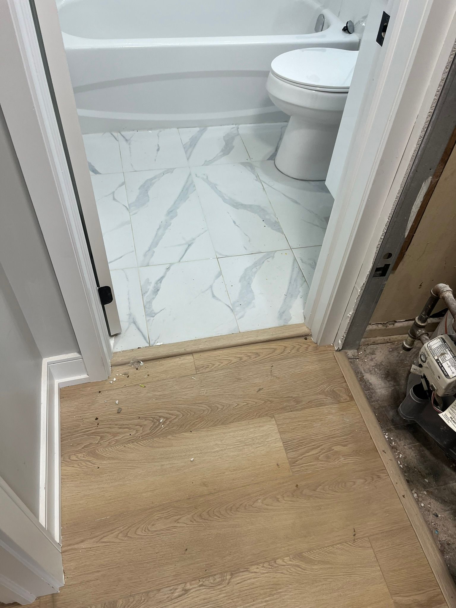 A bathroom with a toilet , bathtub , and wooden floor.