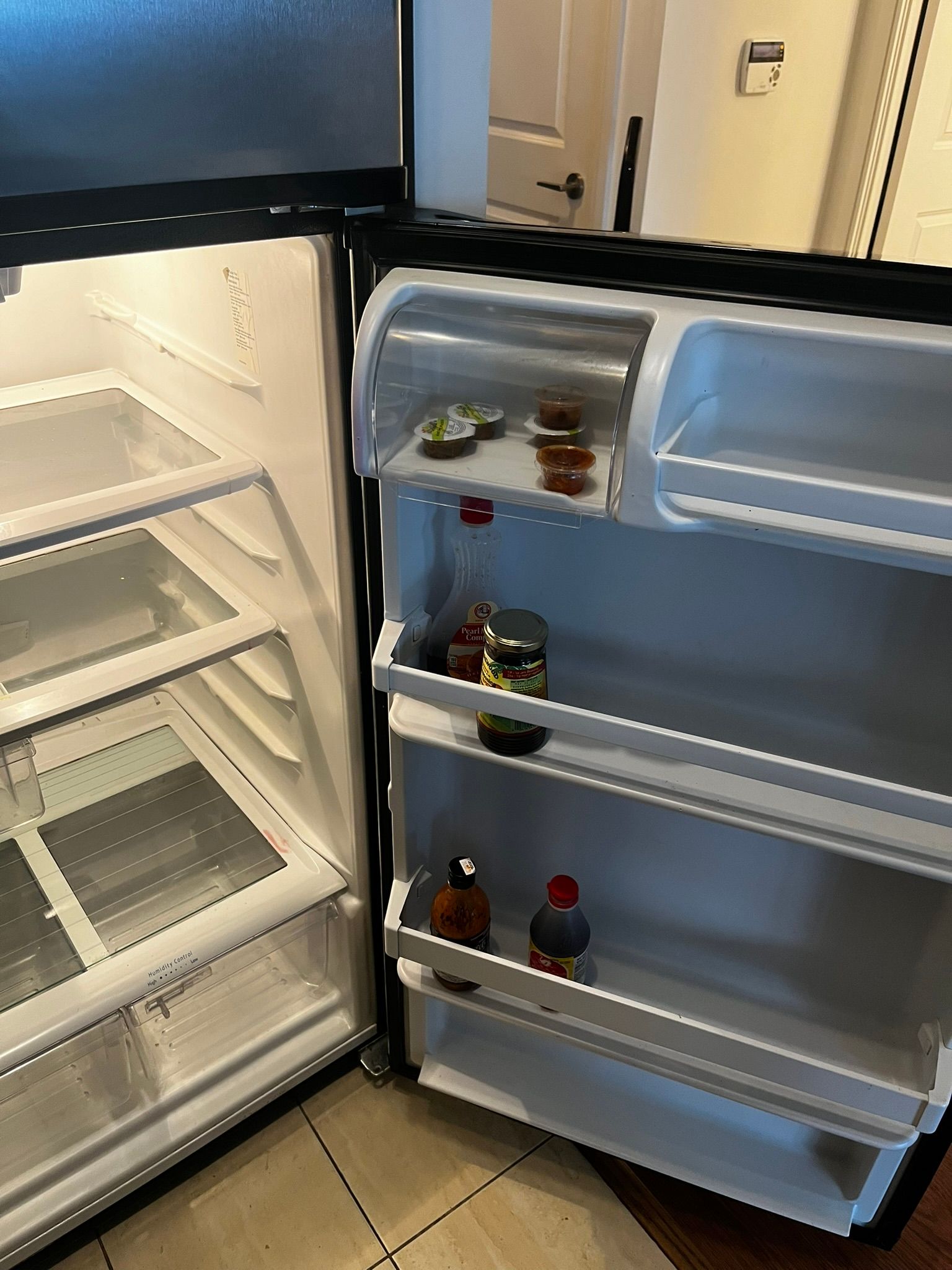 An empty refrigerator with the door open and bottles on the shelves.