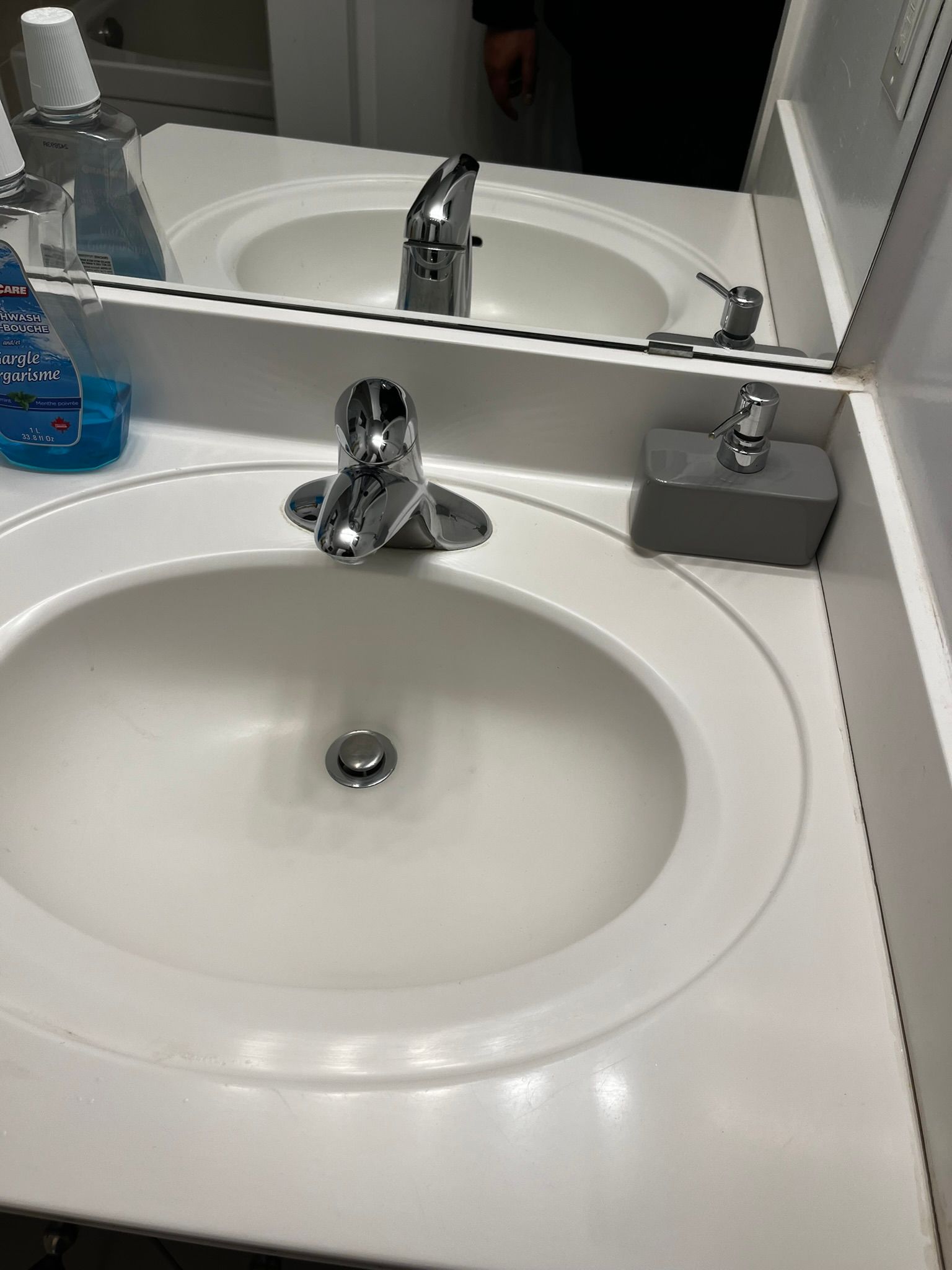 A bathroom sink with a soap dispenser and a mirror.