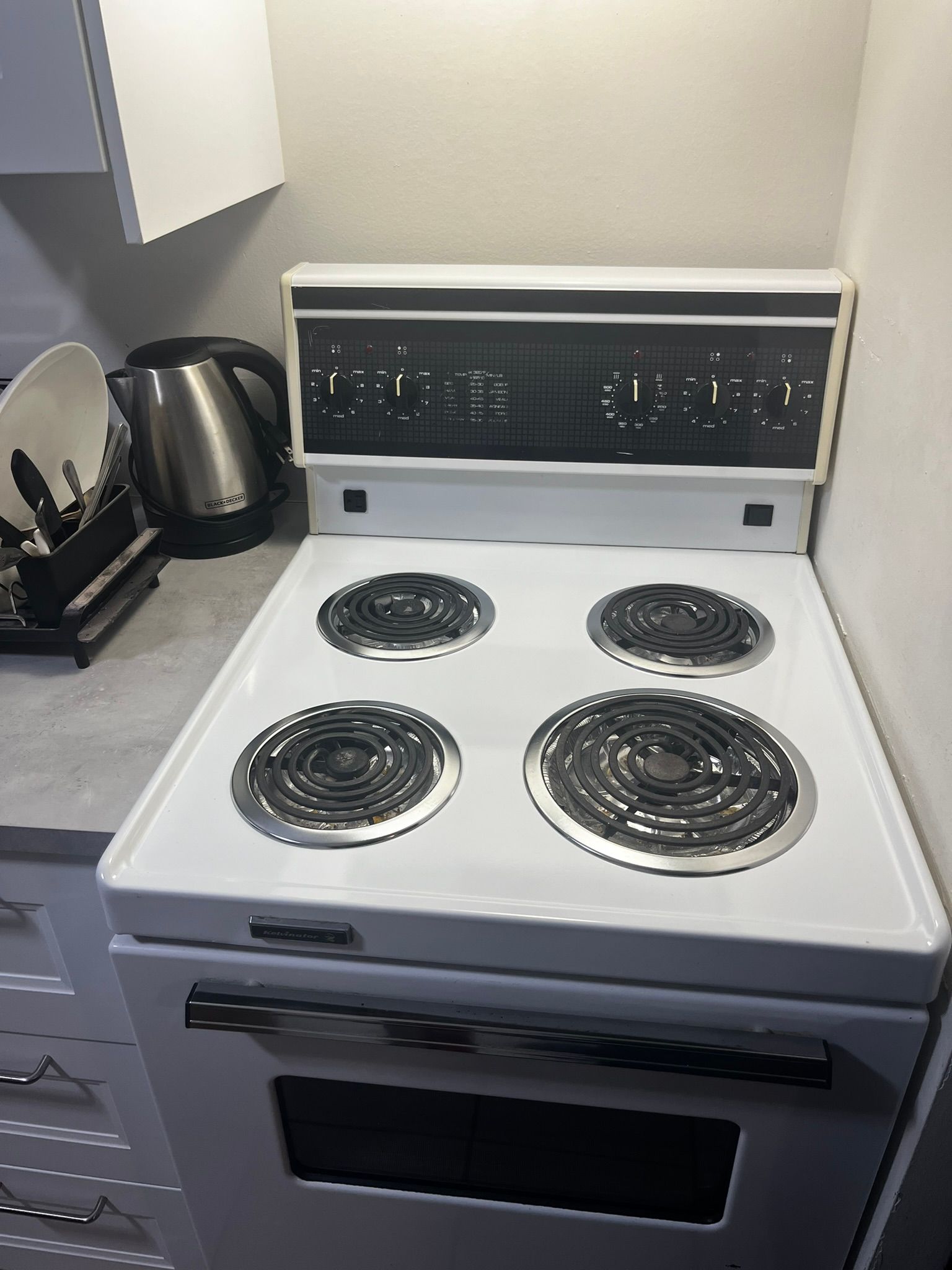 A white electric stove with four burners is sitting on a kitchen counter.