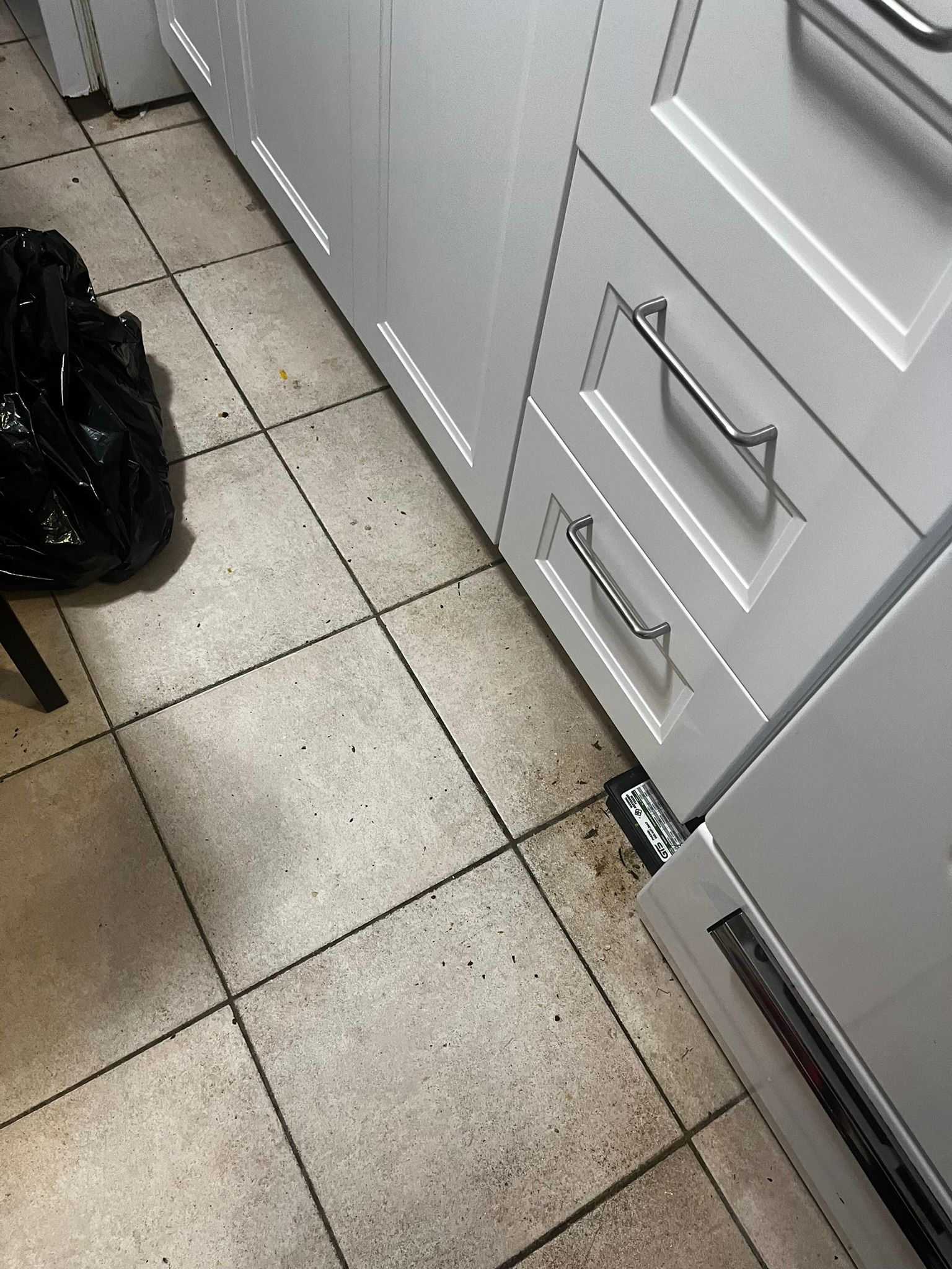 A black bag is sitting on the floor in a laundry room next to a washer and dryer.