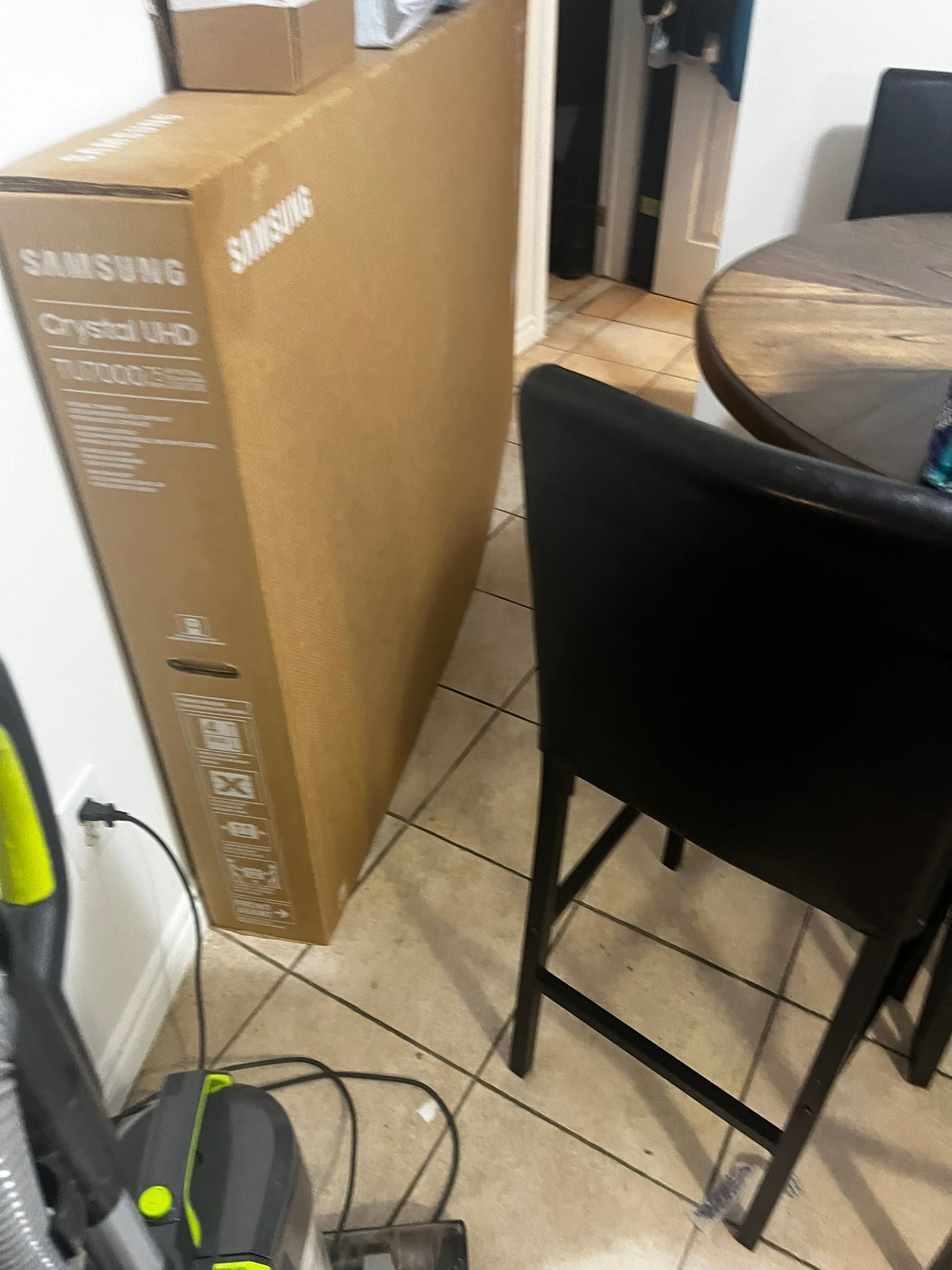 A large cardboard box is sitting on the floor next to a vacuum cleaner.
