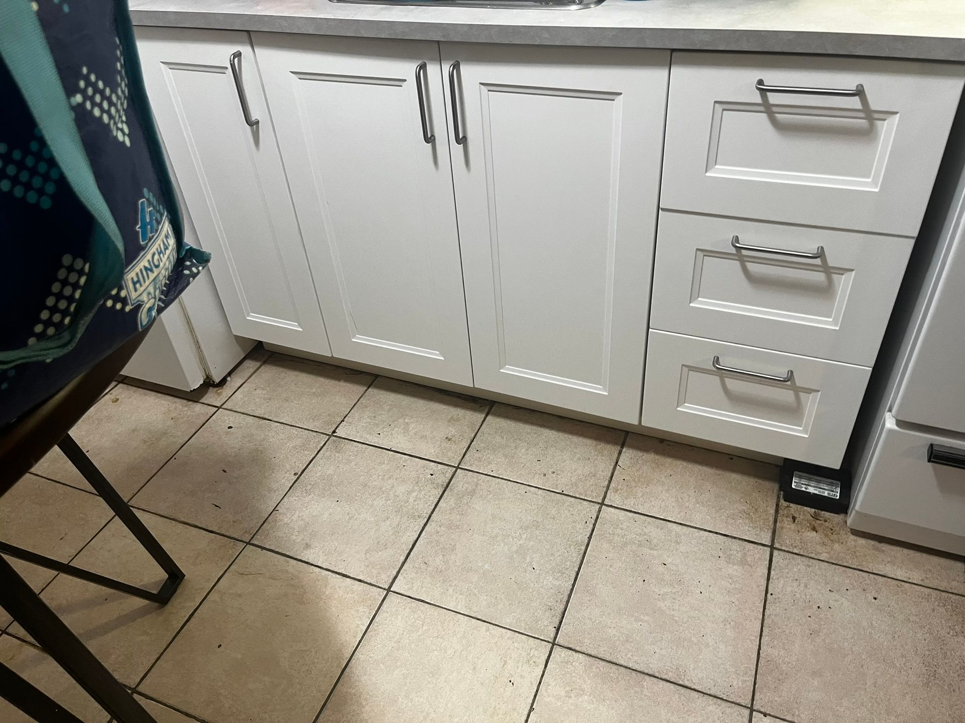 A kitchen with white cabinets and drawers and a tiled floor