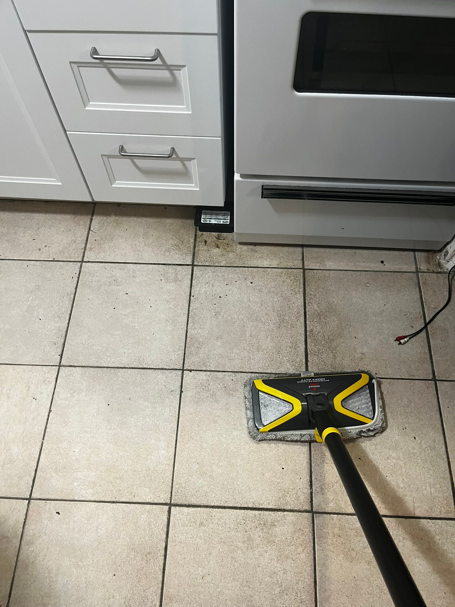 A mop is being used to clean a tiled floor in a kitchen.