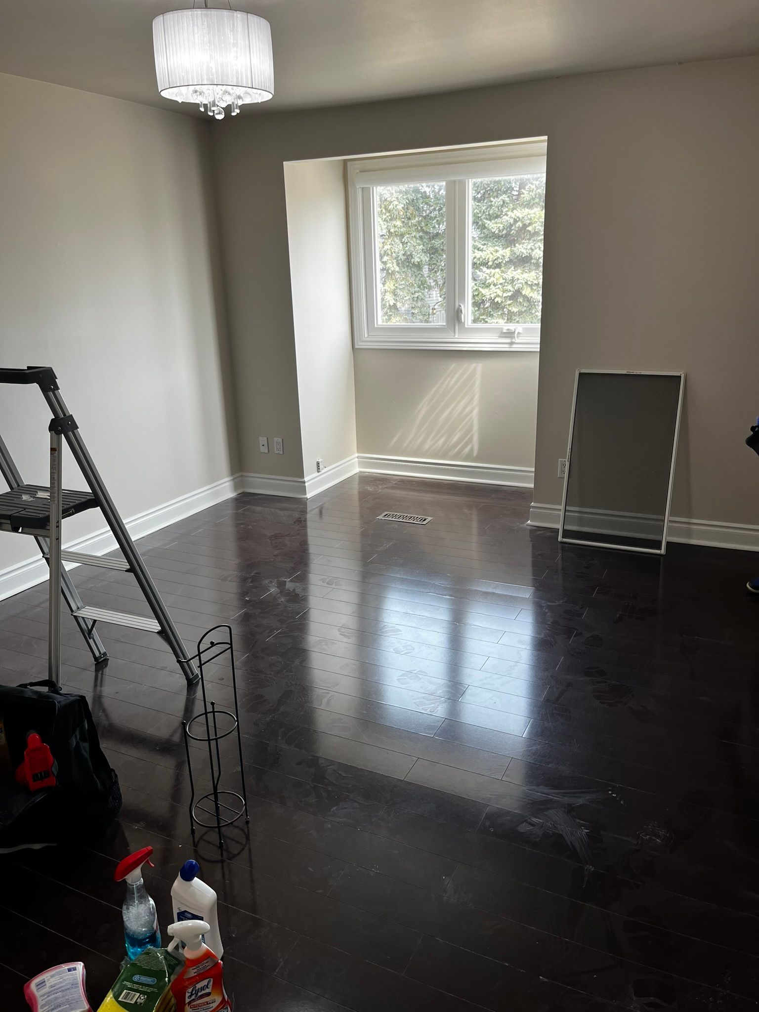 An empty room with a ladder and cleaning supplies on the floor.