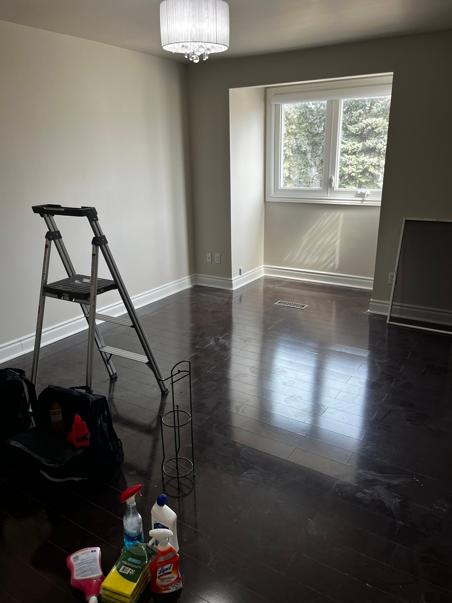 An empty room with a ladder and cleaning supplies on the floor.