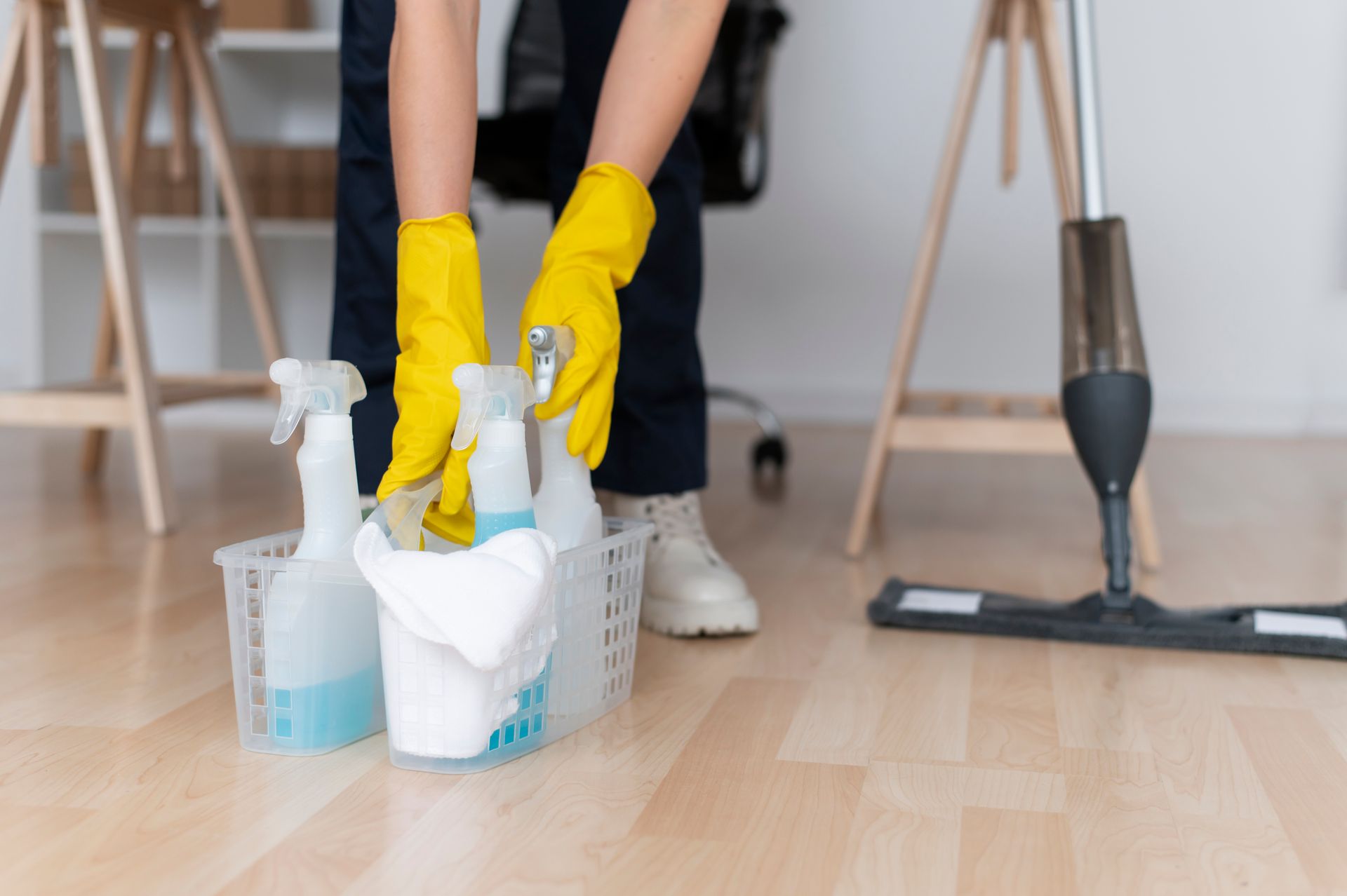 Person in yellow gloves taking cleaning supplies from a basket, near a mop, in an office.