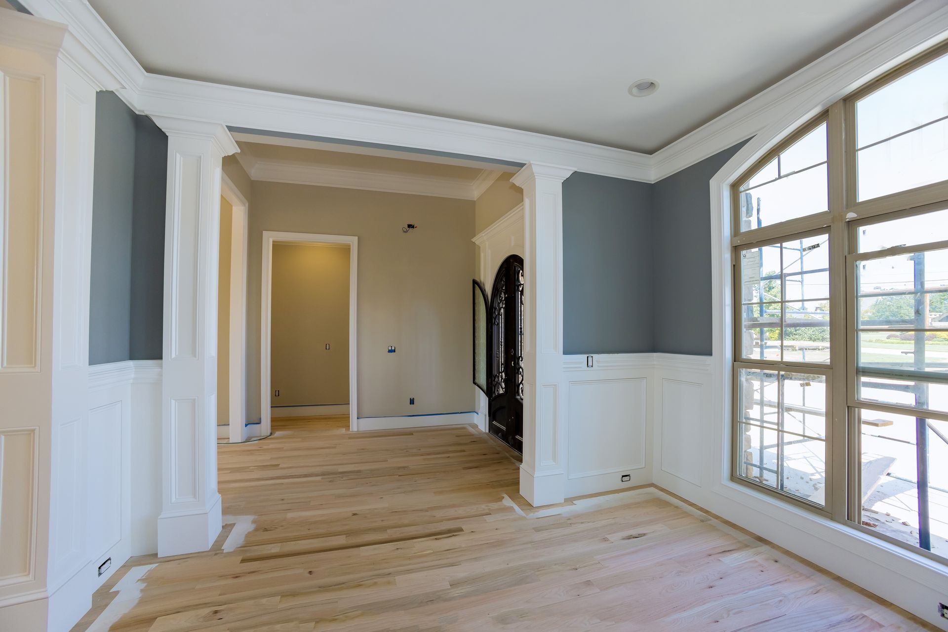 Empty room with unfinished light wood floors, gray and white walls, and large window.
