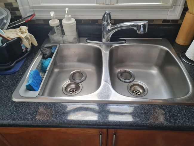 Stainless steel double kitchen sink with faucet, soap dispensers, and sponges.