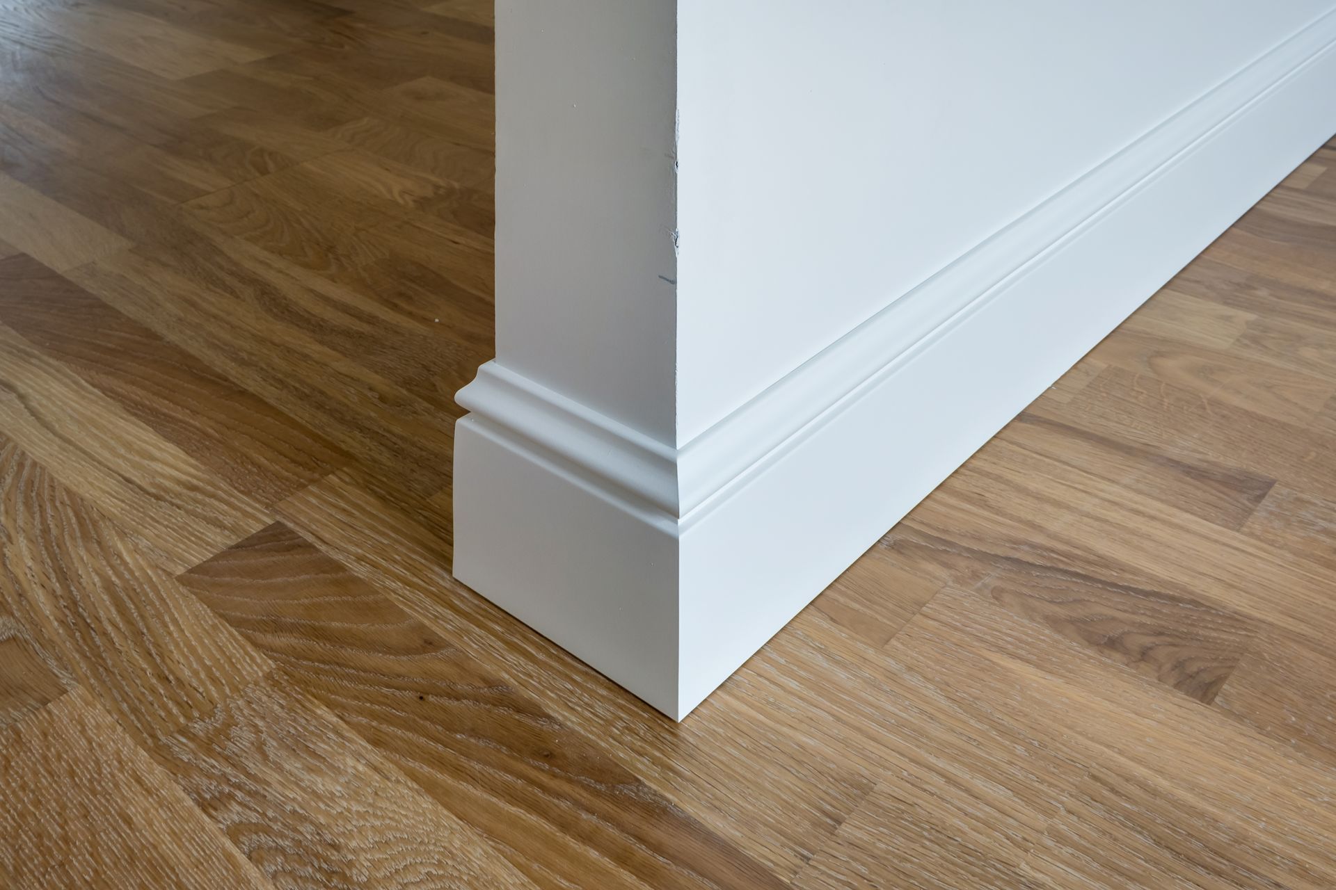 White painted wall corner with decorative baseboard on wood floor.
