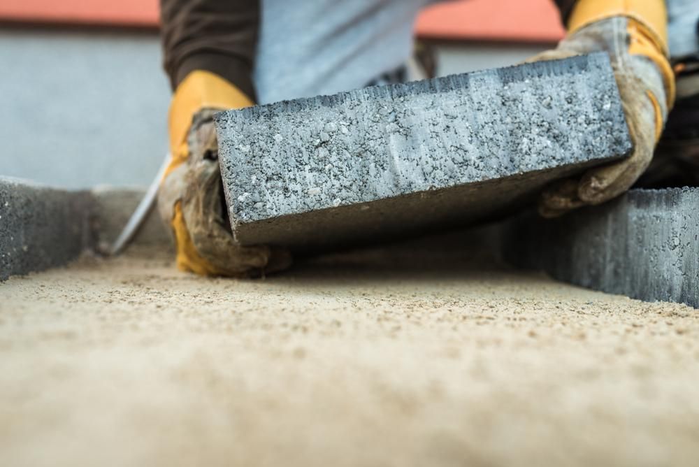 A Man Is Laying Bricks on A Sidewalk — Australian Sandstone Products In Gatton, QLD