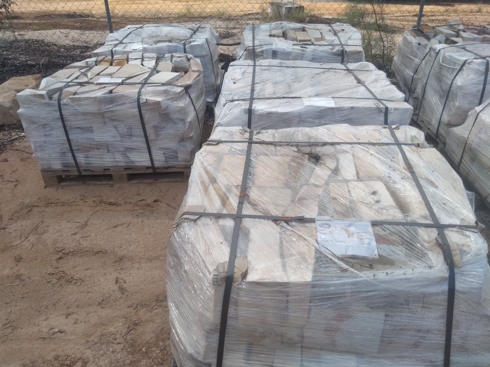Pallets of Stone Pavers, Wrapped in Plastic, Sit on a Sandy Surface — Australian Sandstone Products In Ipswich, QLD