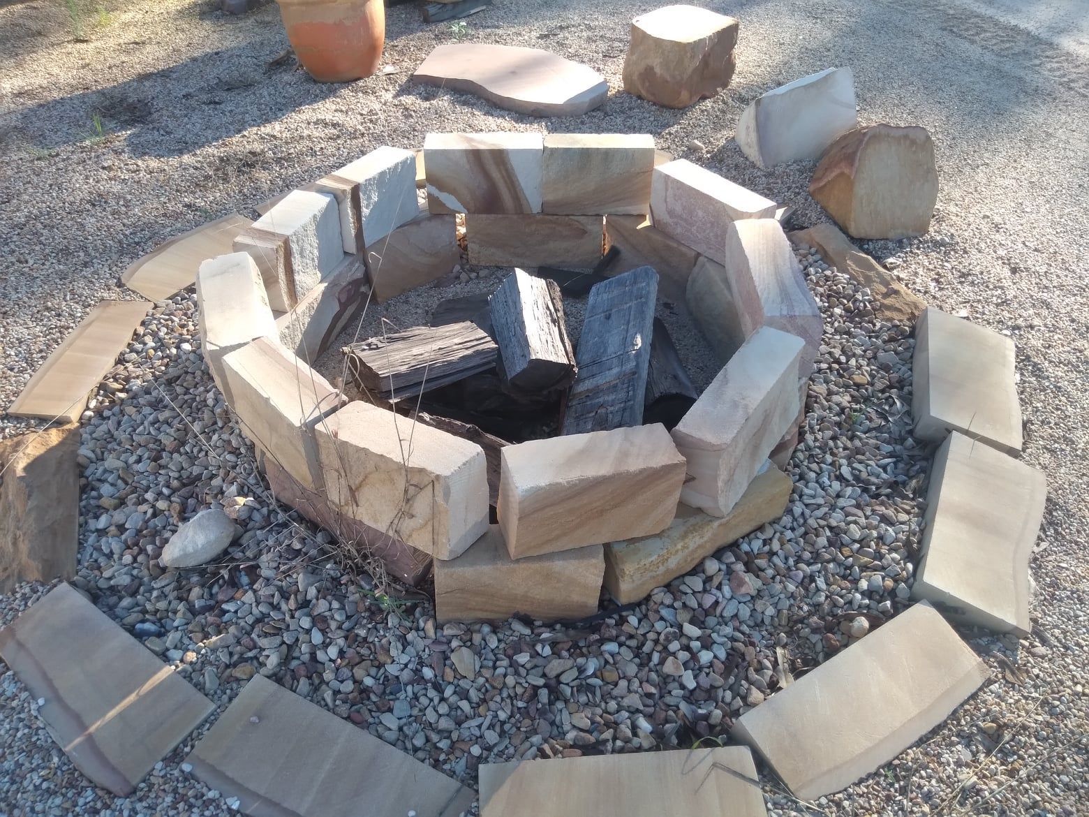 Stone Fire Pit Built in a Gravel Yard, Containing Firewood — Australian Sandstone Products In Ipswich, QLD