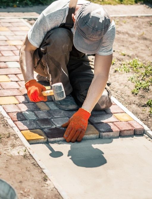 A Man Is Kneeling Down And Laying Bricks On A Sidewalk — Australian Sandstone Products In Helidon, QLD