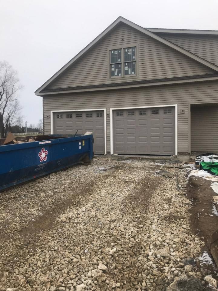 A blue dumpster is parked in front of a house under construction.