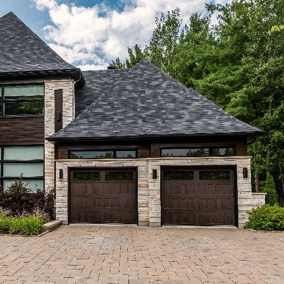 A large house with two garage doors and a brick driveway.