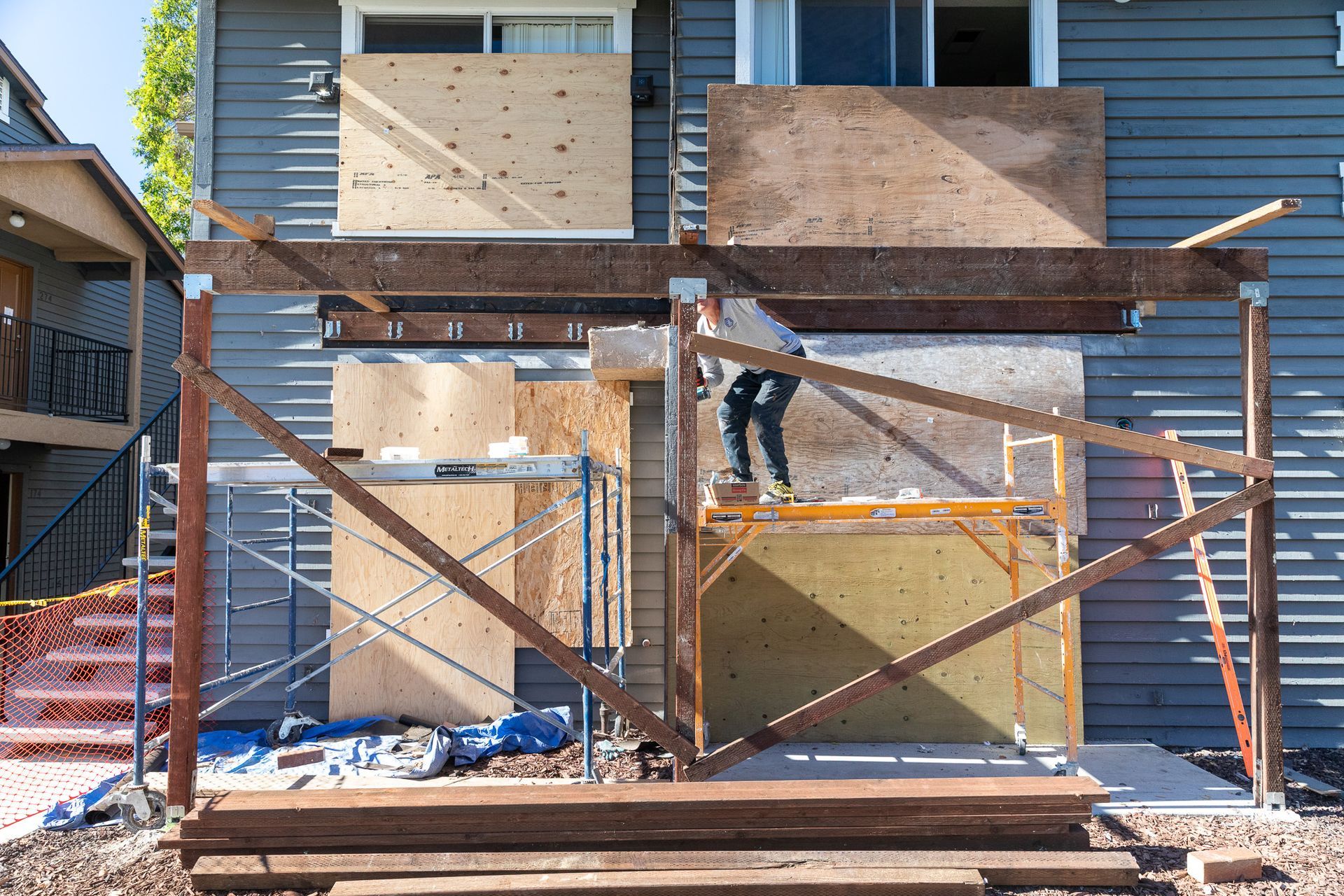 Construction site with person on scaffolding. Building has plywood over windows. Brown wood framing in place.